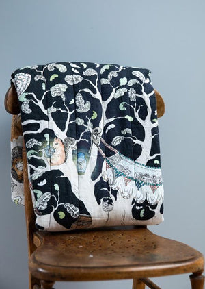 Hand illustrated nighttime woodland scene quilted blanket folded up on a wooden chair.