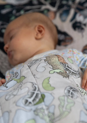 A baby asleep under a reversible woodland scene quilted blanket.
