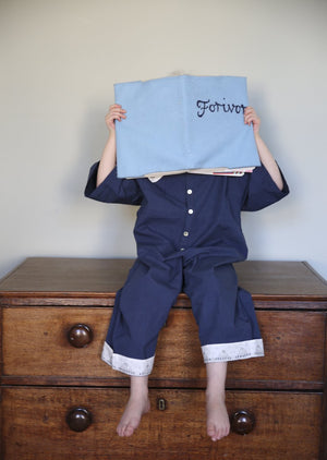 Child sitting on a chest of drawers holding a Forivor branded journal wearing nighttime blue jumpsuit.