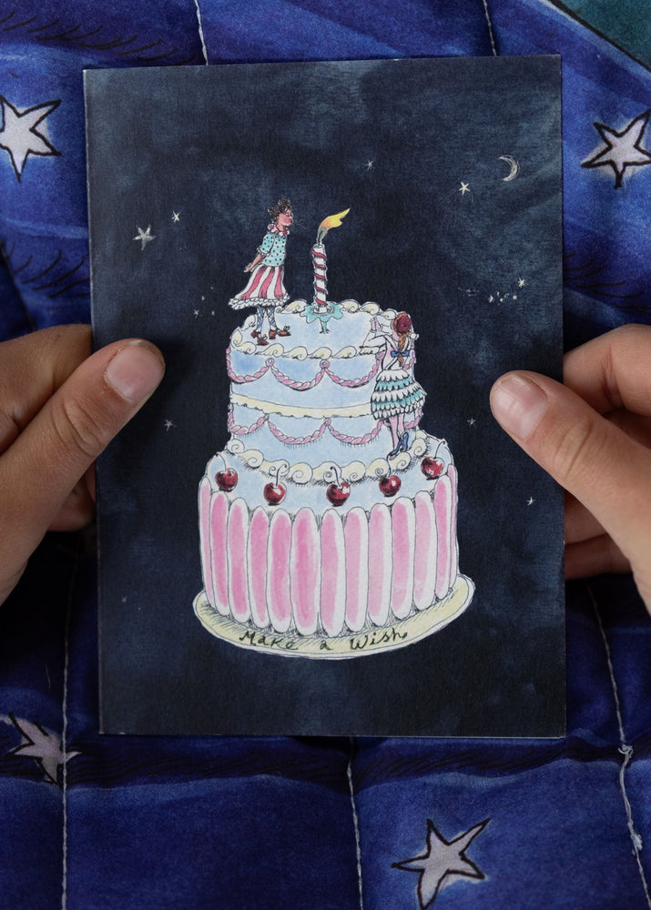 Person holding a card with a cake illustration against a blue quilted background.