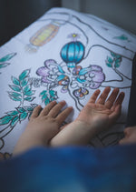 Close up of child's hands on the corner of a white organic cotton fitted sheet featuring flowers, branches and lanterns.
