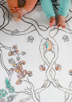 Two pairs of babies bare feet on top of an organic white fitted cot sheet with a hand illustrated design of nuthatch birds, flowers, branches and lanterns.