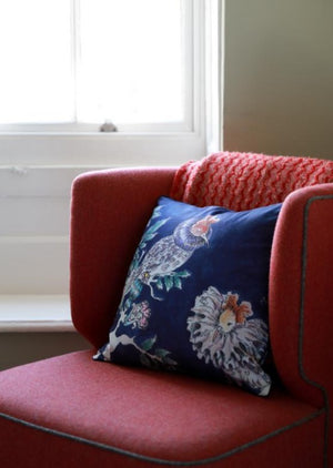 A square blue cushion featuring two hand illustrated ruff birds on a red felt covered chair.