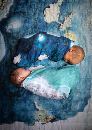 Two newborn twin babies wrapped in reversible underwater scene muslin blankets.