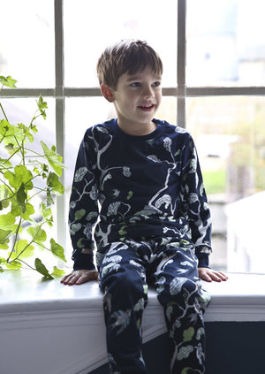 A little boy sitting on a windowsill wearing woodland scene blue cotton pyjamas.