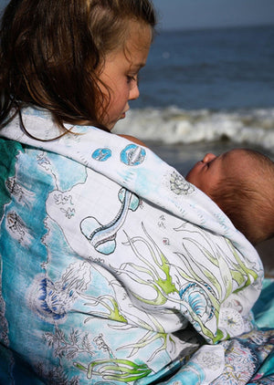 A girl and newborn baby wrapped in our organic muslin swaddle.